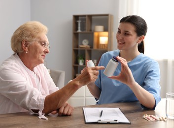 Photo of Nurse giving pills to senior woman at wooden table indoors. Home health care service