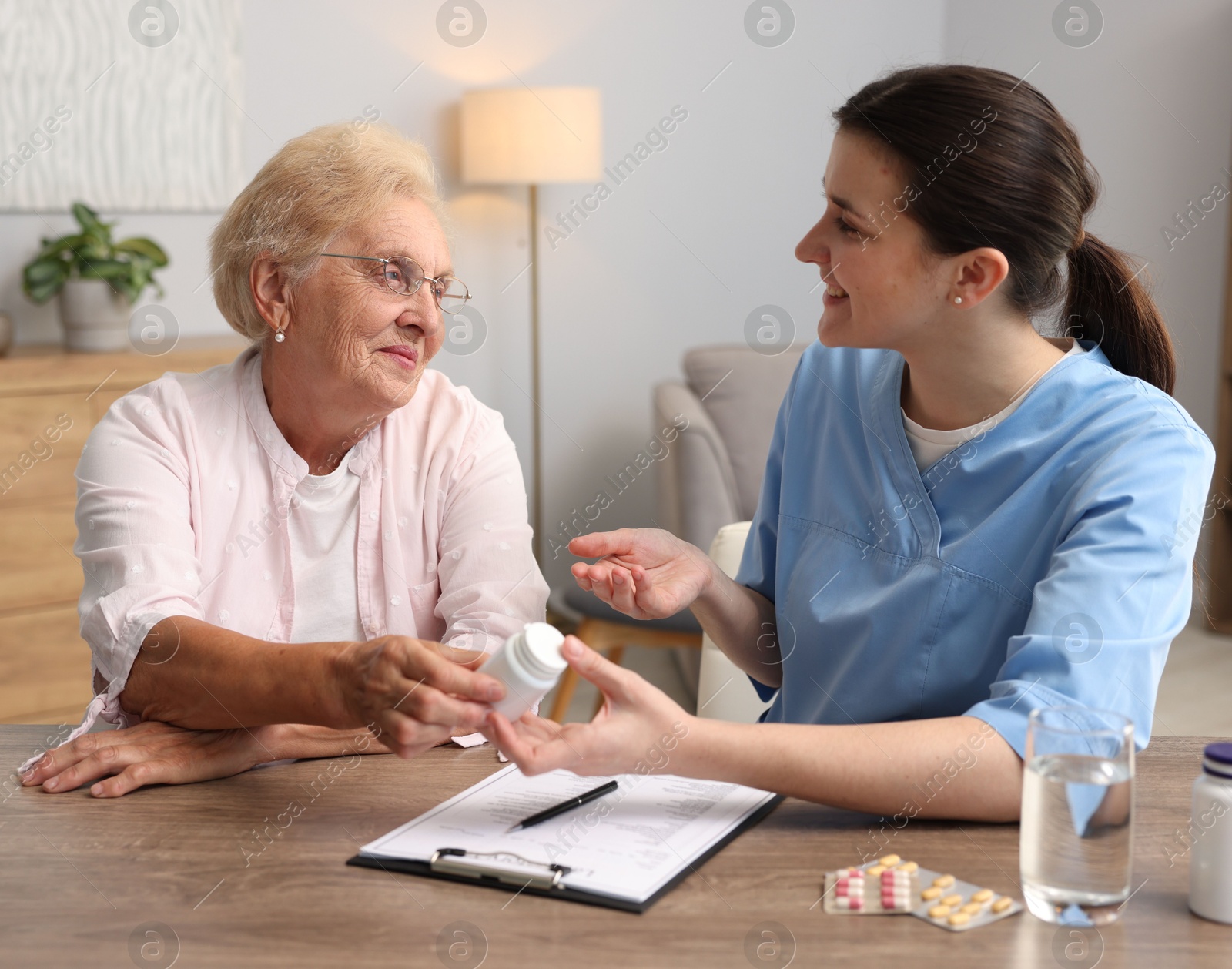 Photo of Nurse giving pills to senior woman at wooden table indoors. Home health care service