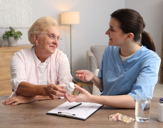 Photo of Nurse giving pills to senior woman at wooden table indoors. Home health care service