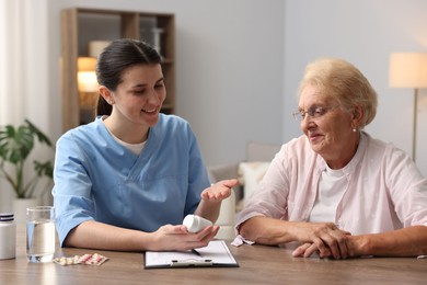 Photo of Nurse giving pills to senior woman at wooden table indoors. Home health care service
