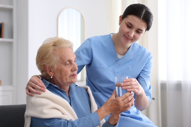 Photo of Nurse giving glass of water to senior woman indoors. Home health care service
