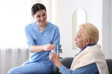 Photo of Nurse giving glass of water to senior woman indoors. Home health care service