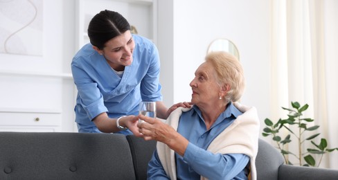 Photo of Nurse giving glass of water to senior woman indoors. Home health care service