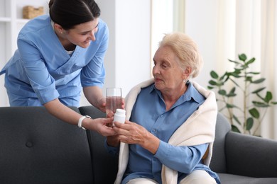 Photo of Nurse giving glass of water and pills to senior woman indoors. Home health care service