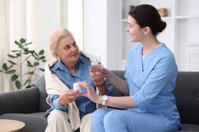 Photo of Nurse giving glass of water and pills to senior woman indoors. Home health care service