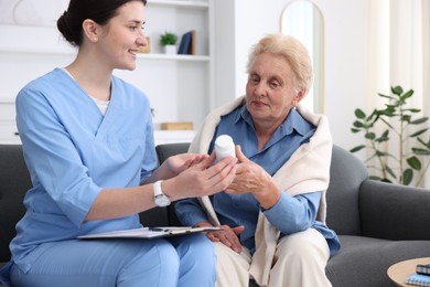 Photo of Nurse giving pills to senior woman indoors. Home health care service