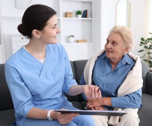 Photo of Nurse with clipboard examining senior woman indoors. Home health care service