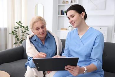 Photo of Nurse with clipboard examining senior woman indoors. Home health care service