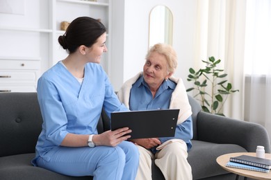 Photo of Nurse with clipboard examining senior woman indoors. Home health care service