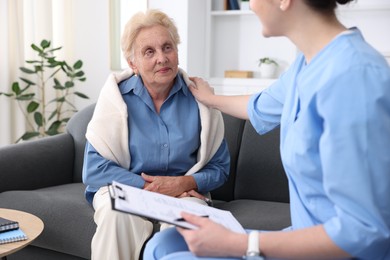 Photo of Nurse with clipboard examining senior woman indoors, closeup. Home health care service