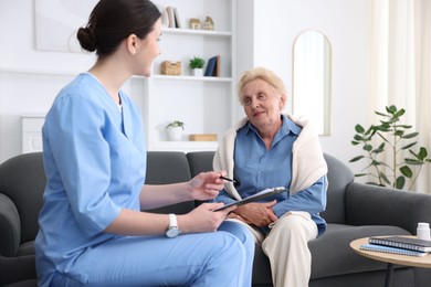 Photo of Nurse with clipboard examining senior woman indoors. Home health care service