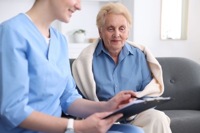 Photo of Nurse with clipboard examining senior woman indoors, closeup. Home health care service