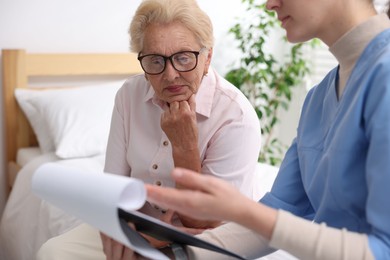 Photo of Nurse with clipboard examining senior woman indoors, closeup. Home health care service