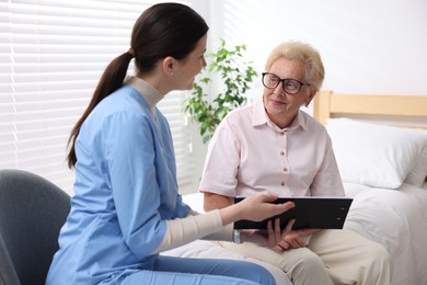 Photo of Nurse with clipboard examining senior woman indoors. Home health care service