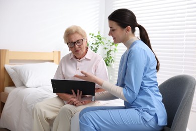 Photo of Nurse with clipboard examining senior woman indoors. Home health care service