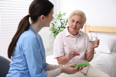 Photo of Nurse giving pills to senior woman indoors. Home health care service