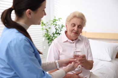 Photo of Nurse giving glass of water to senior woman indoors, selective focus. Home health care service