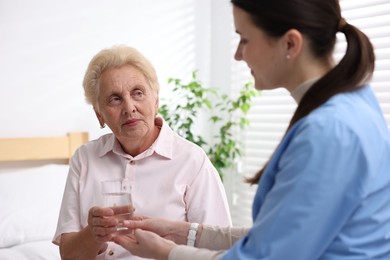 Photo of Nurse giving glass of water to senior woman indoors, selective focus. Home health care service
