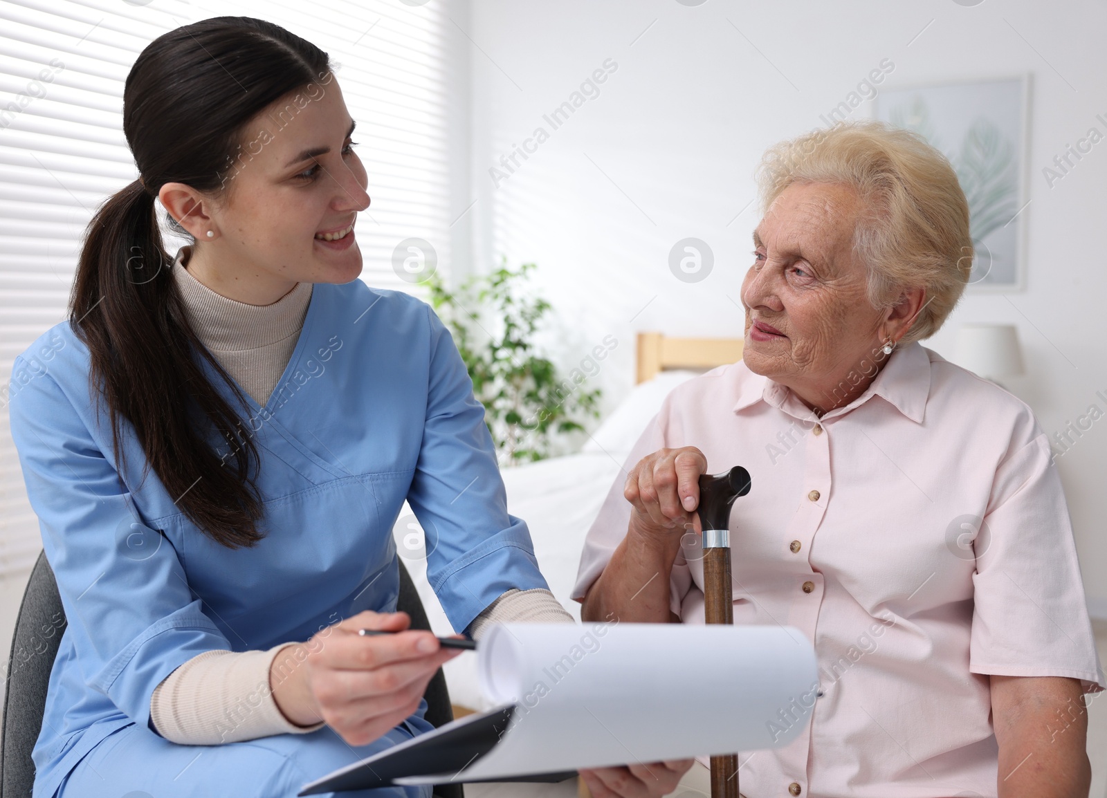 Nurse with clipboard examining senior woman indoors. Home health care service Photo of Nurse with clipboard examining senior woman indoors. Home health care service