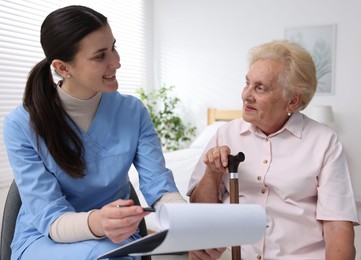 Photo of Nurse with clipboard examining senior woman indoors. Home health care service