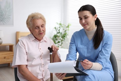 Photo of Nurse with clipboard examining senior woman indoors. Home health care service