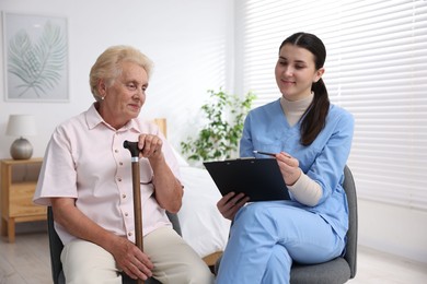 Photo of Nurse with clipboard examining senior woman indoors. Home health care service