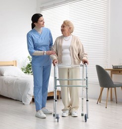 Photo of Nurse assisting senior woman with walking frame indoors. Home health care service