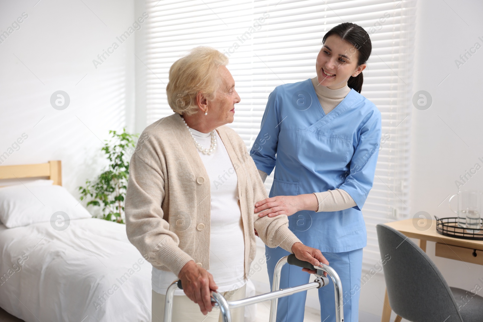Photo of Nurse assisting senior woman with walking frame indoors. Home health care service