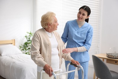 Photo of Nurse assisting senior woman with walking frame indoors. Home health care service