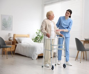 Photo of Nurse assisting senior woman with walking frame indoors. Home health care service