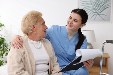 Photo of Nurse with clipboard examining senior woman indoors. Home health care service
