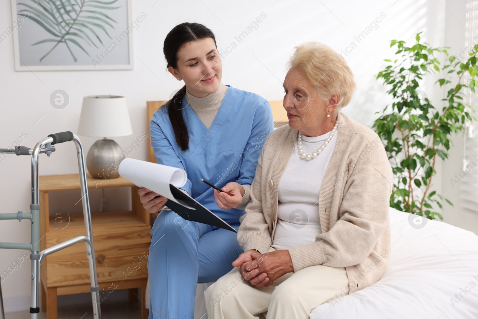 Photo of Nurse with clipboard examining senior woman indoors. Home health care service