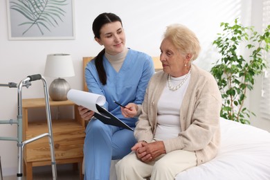 Photo of Nurse with clipboard examining senior woman indoors. Home health care service