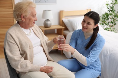 Photo of Nurse giving water to senior woman on sofa indoors. Home health care service