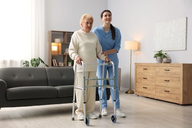 Photo of Nurse assisting senior woman with walking frame indoors. Home health care service
