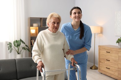 Photo of Nurse assisting senior woman with walking frame indoors. Home health care service