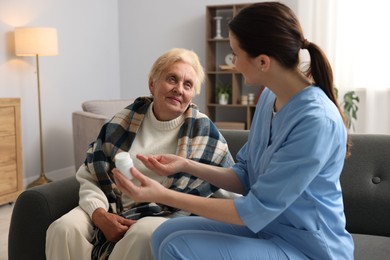 Photo of Nurse giving water to senior woman on sofa indoors. Home health care service