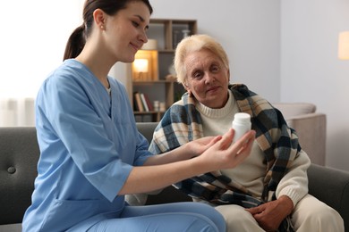 Photo of Nurse giving water to senior woman on sofa indoors. Home health care service