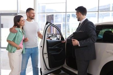 Photo of Salesman with clipboard showing new car to happy family in salon