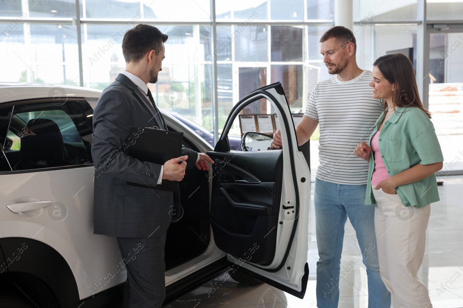 Salesman with clipboard showing new car to happy family in salon Photo of Salesman with clipboard showing new car to happy family in salon