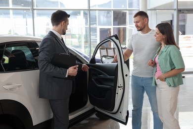 Photo of Salesman with clipboard showing new car to happy family in salon