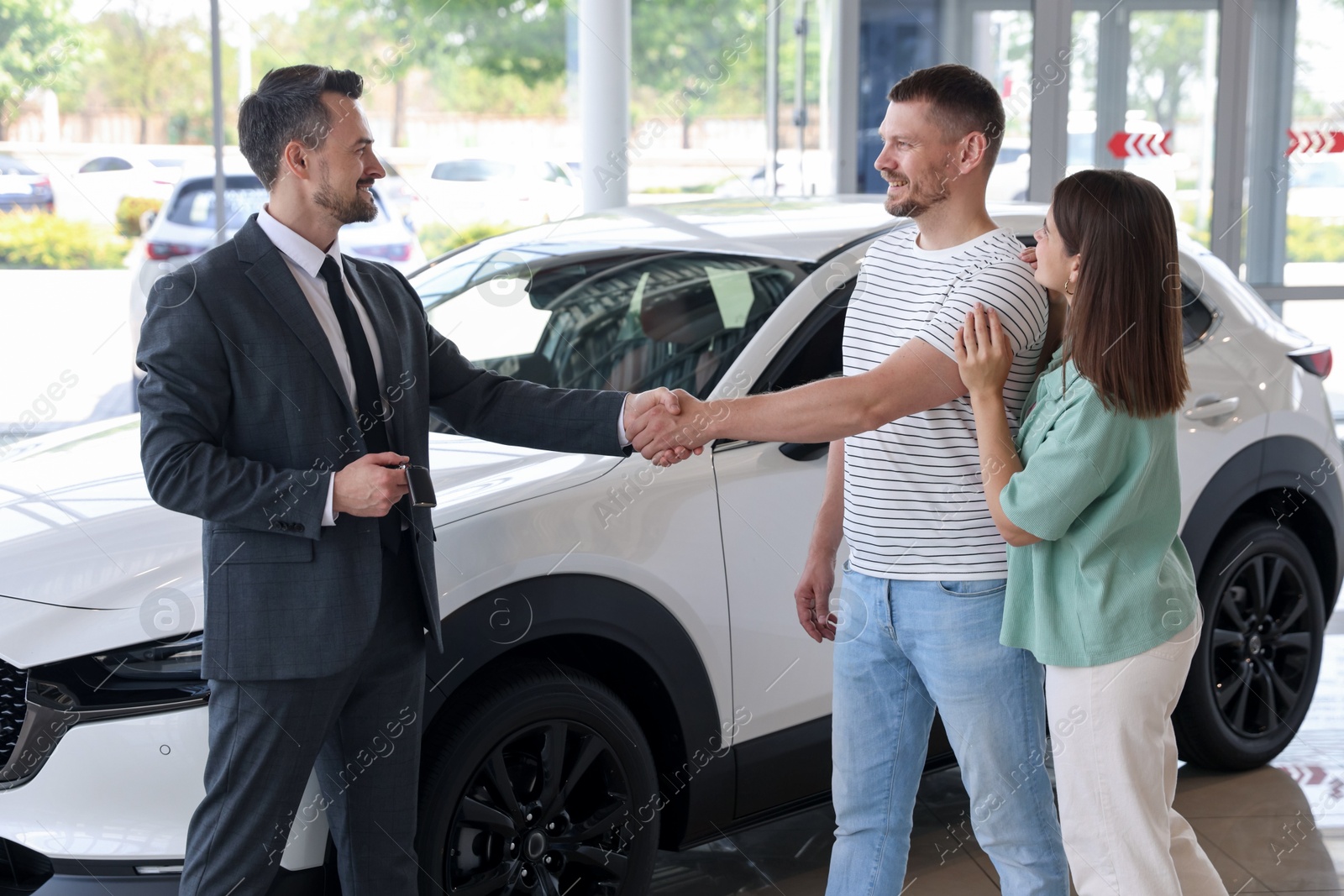 Salesman shaking hands with happy family near new car in salon Photo of Salesman shaking hands with happy family near new car in salon