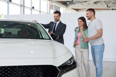 Photo of Salesman showing new car to happy family in salon