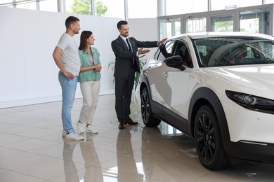 Photo of Salesman showing new car to happy family in salon