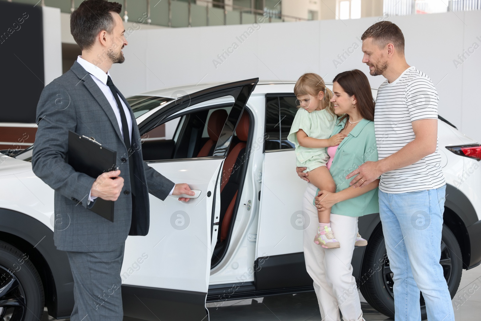 Salesman with clipboard showing new car to happy family in salon Photo of Salesman with clipboard showing new car to happy family in salon