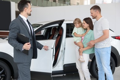 Photo of Salesman with clipboard showing new car to happy family in salon