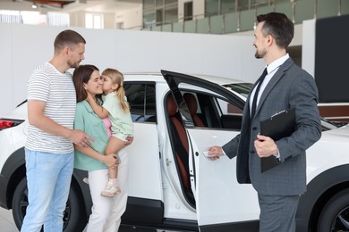 Photo of Salesman with clipboard showing new car to happy family in salon