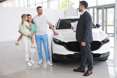 Photo of Salesman with clipboard showing new car to happy family in salon