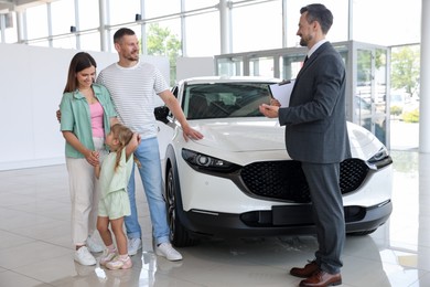 Photo of Salesman with clipboard showing new car to happy family in salon