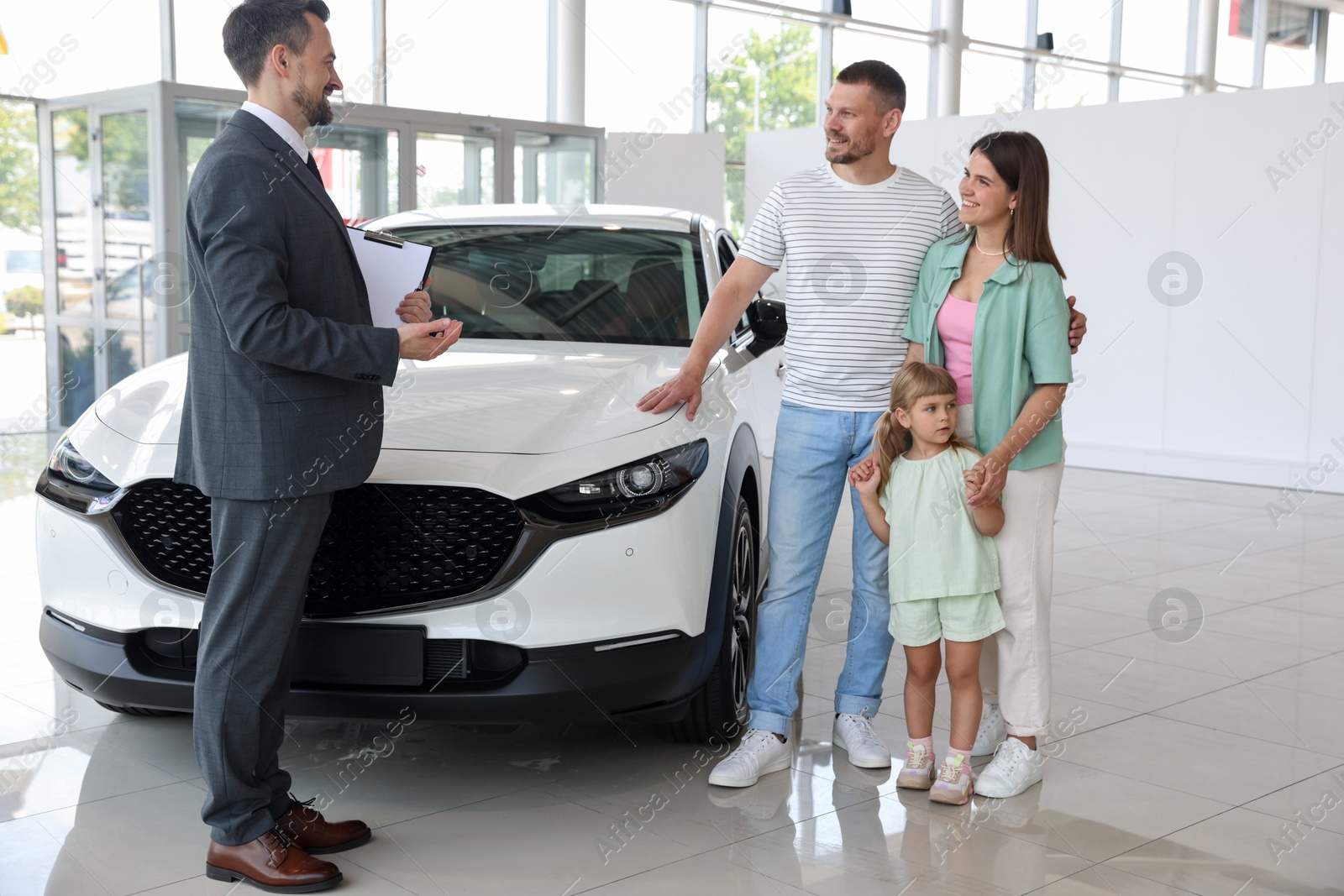 Salesman with clipboard showing new car to happy family in salon Photo of Salesman with clipboard showing new car to happy family in salon